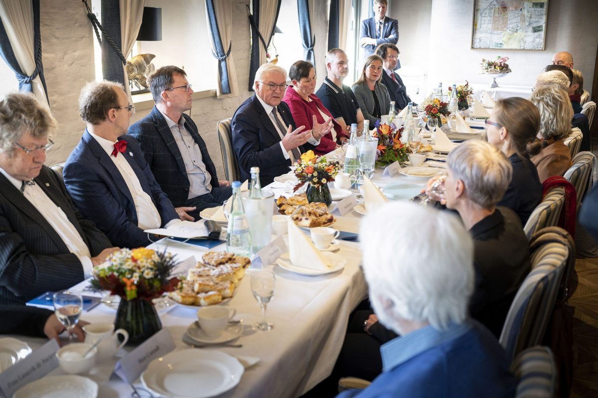 Bundespräsident sitzt mit etwa zehn Menschen an einer Tafel und spricht